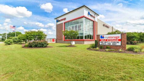 Front view of a self-storage facility with a well-maintained entrance, clear signage, and surrounding green landscape.