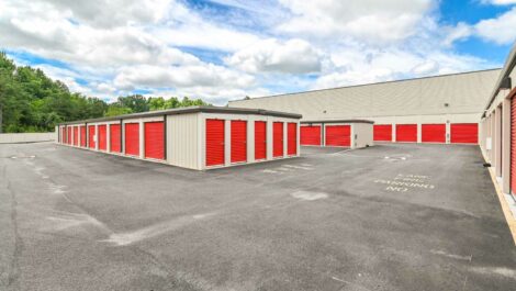 Exterior view of a self-storage facility with a spacious driveway and neatly aligned storage units under a clear sky.