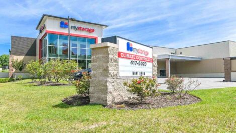 Wide-angle view of a self-storage facility with a clean, spacious parking area and multiple storage units, set against a bright, clear sky.