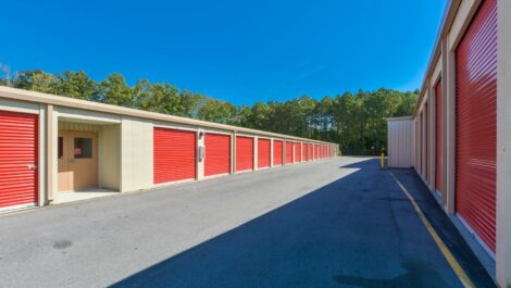 Front view of a self-storage facility with multiple storage units, surrounded by green landscaping and a clear blue sky.