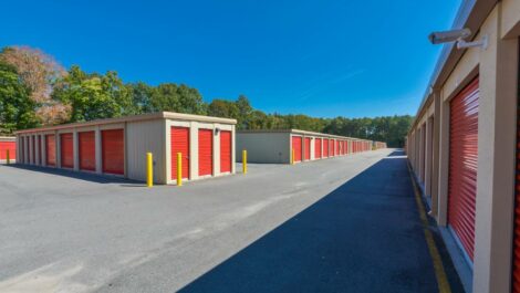 Wide-angle shot of a self-storage facility with multiple units and a large, open driveway under a clear blue sky.