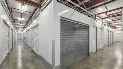 Exterior view of a self-storage facility with modern architecture, featuring multiple storage units and a clean, well-maintained driveway under a clear sky.