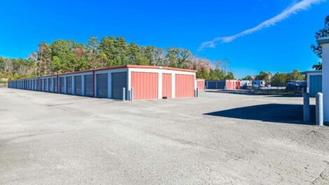 Exterior of a self-storage facility with a spacious driveway, surrounded by green landscaping and under a clear sky.