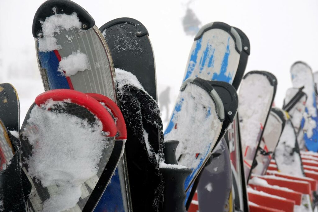 An array of snowy skis on a rack outdoors.