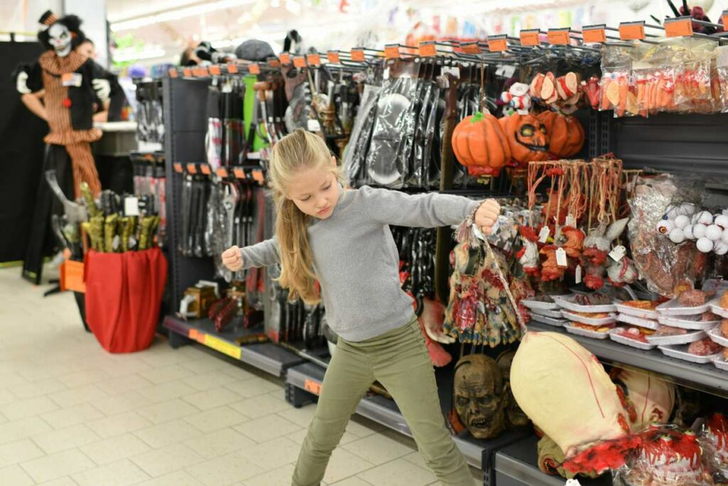 A little girl in a Halloween store playing with a fake severed head.