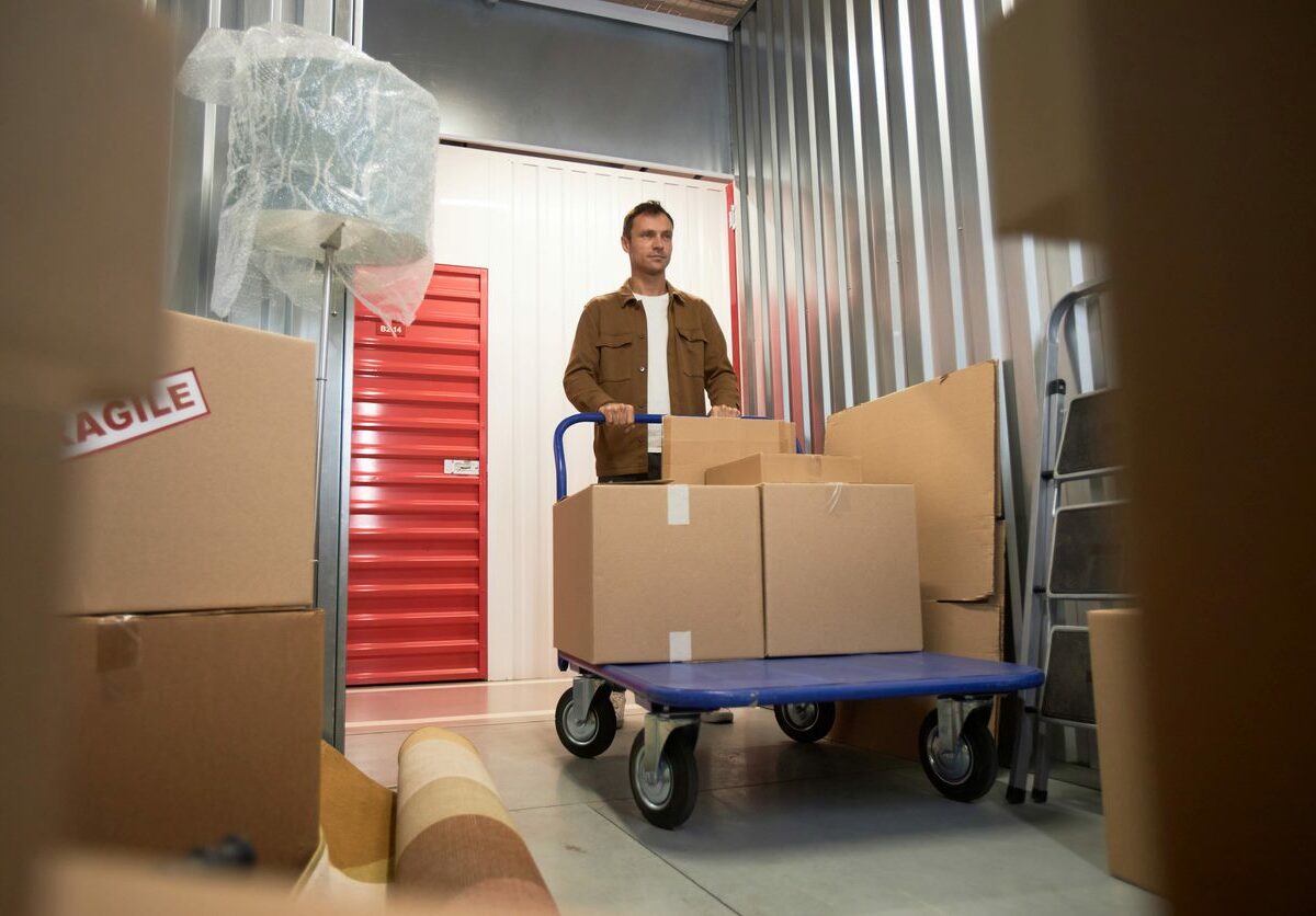 A man pushing a cart of sealed boxes into a storage unit.