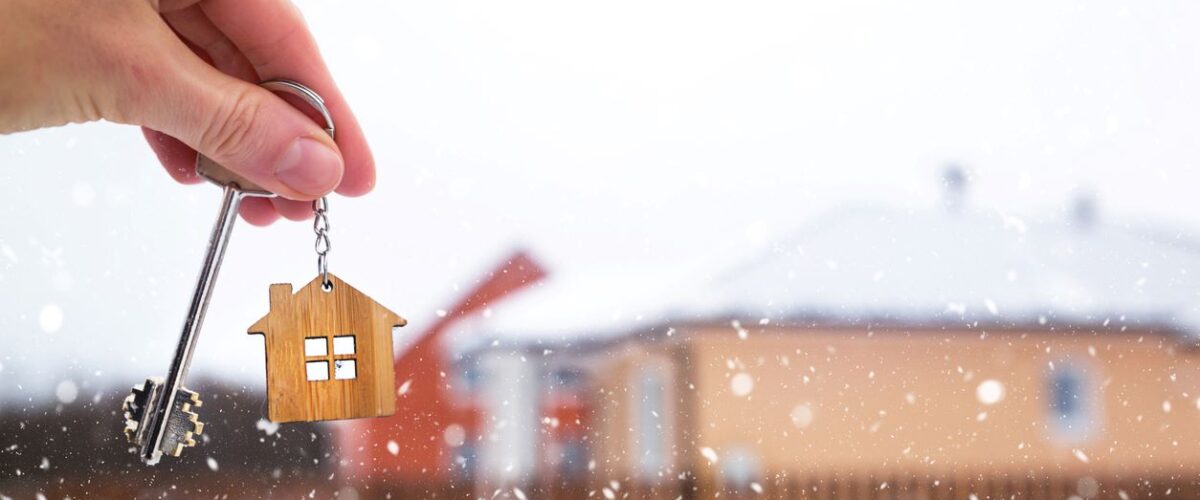 A hand holding a key in front of a house while it snows.