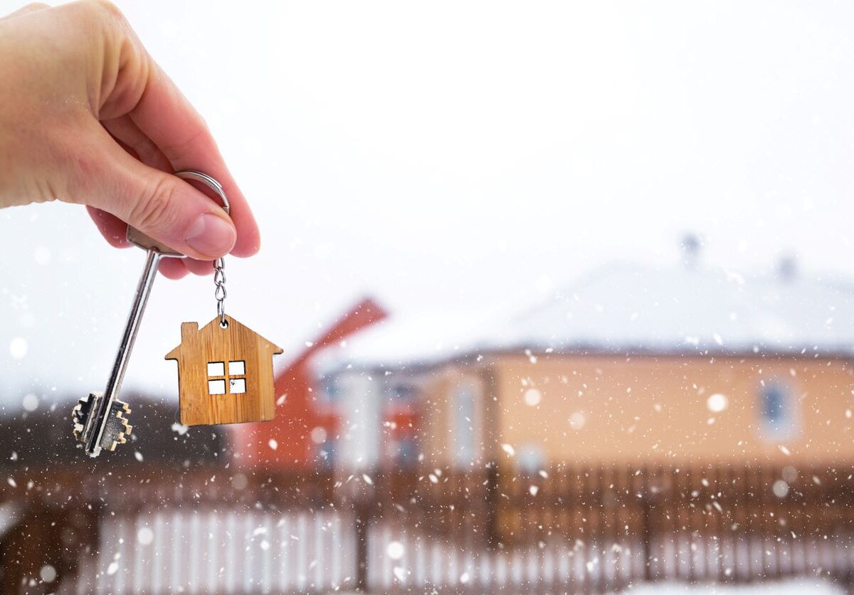 A hand holding a key in front of a house while it snows.