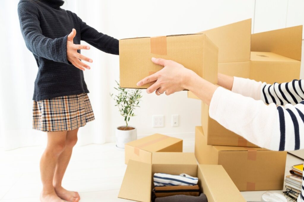 A child and parent packing their belongings in cardboard boxes for a move.