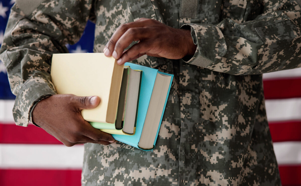 A soldier holding books with the United States flag in the background.