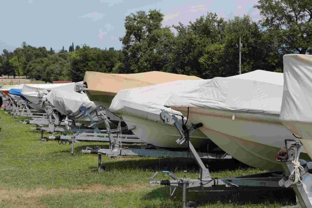 A row of covered boats in a grassy lot.