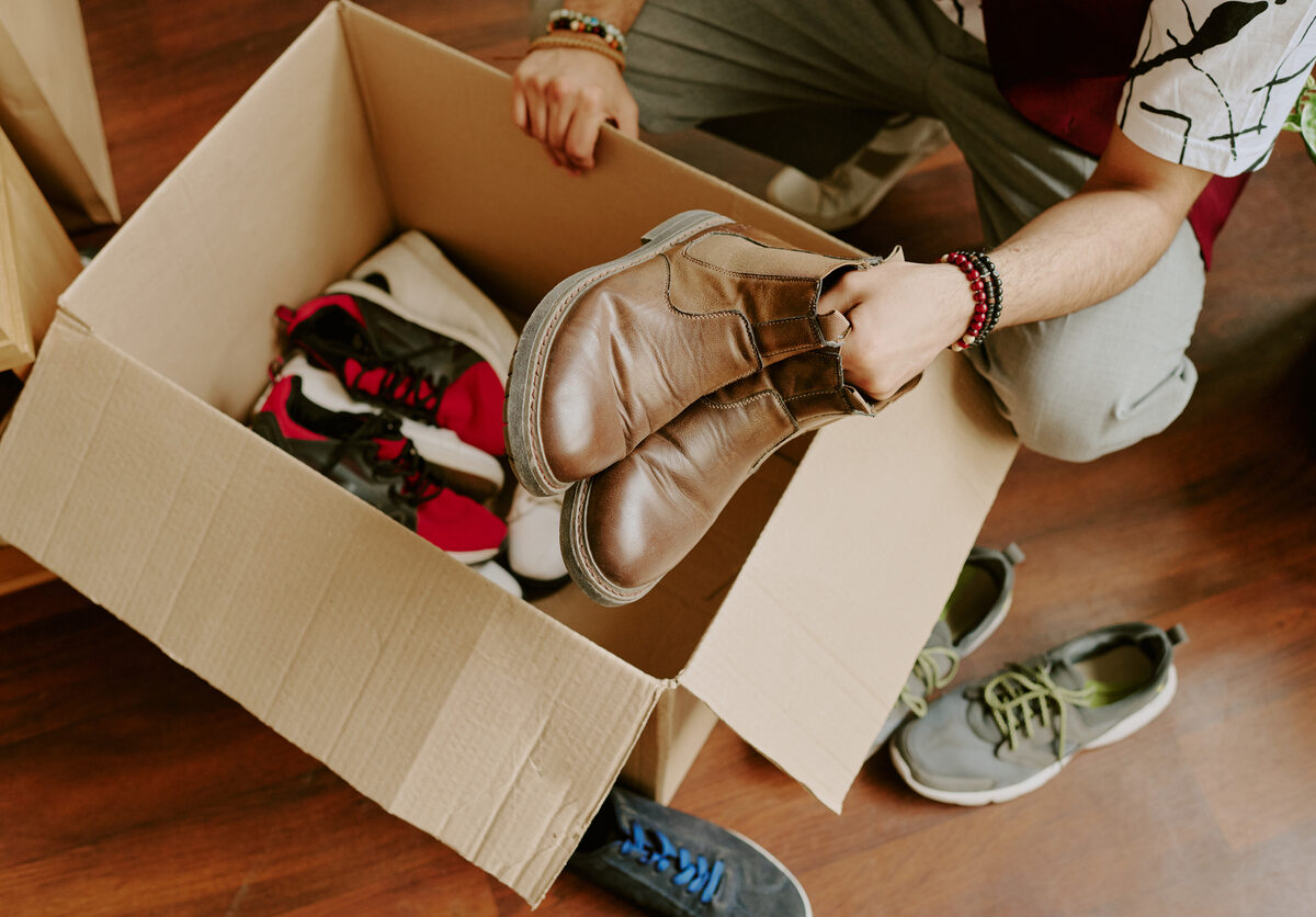 A man packs seasonal clothing and shoes into a cardboard box for storage.