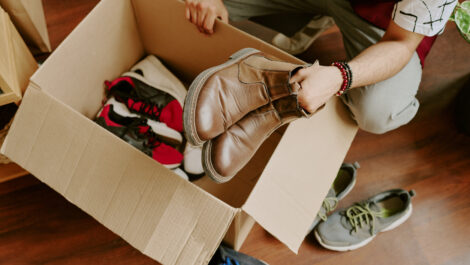 A man packs seasonal clothing and shoes into a cardboard box for storage.