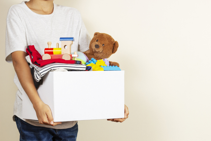 A boy carries a box of toys and clothes, looking for a place to store them.
